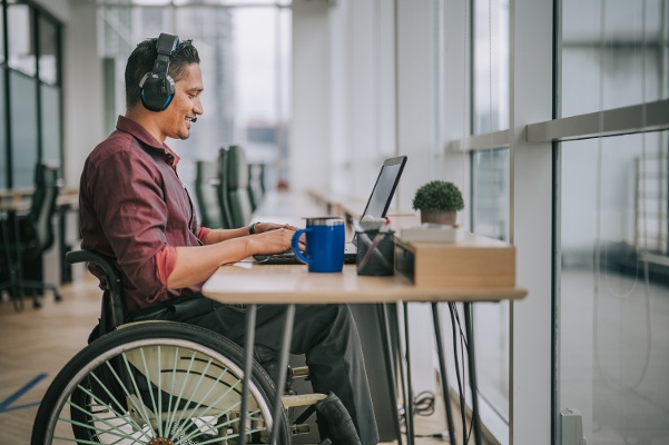 A man in a wheelchair working on a laptop in an office.